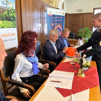 Vertreter sitzen  im historischen Ratssaal der Stadt Treuen als der LEADER-Kooperationsvertrag unterzeichnet wird. Landrat Rolf Keil unterschreibt auf einem Feuerwehrhelm der Jugendfeuerwehr Eich.
